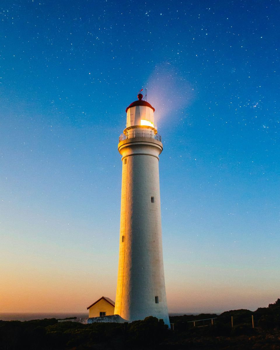 A lighthouse on the Atlantic coast lit at dusk, a steady guiding light