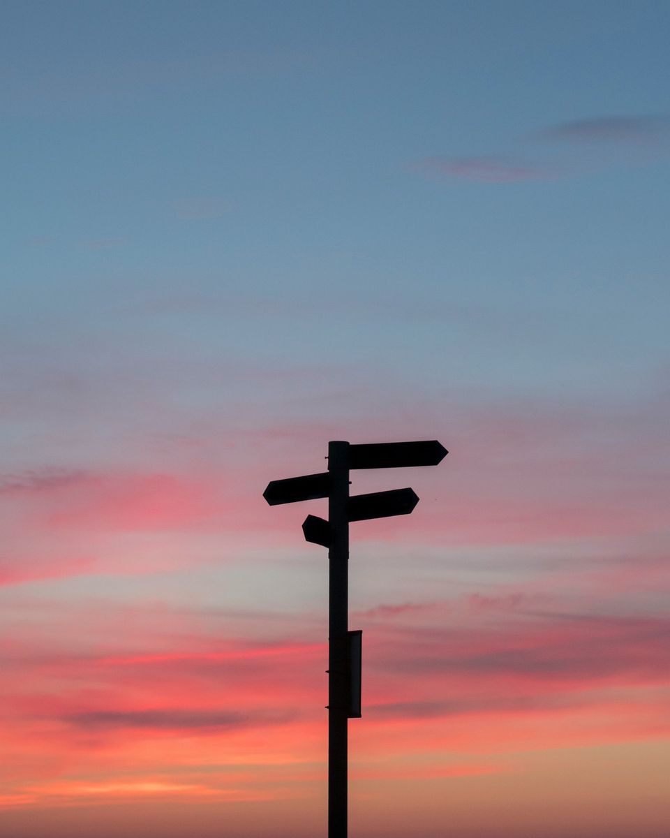 A signpost pointing in several directions against a sunset sky