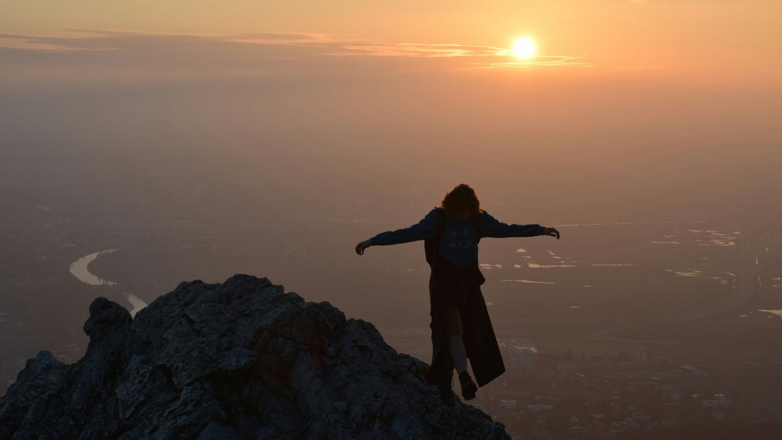 A person stepping carefully along a ridge toward a sunrise